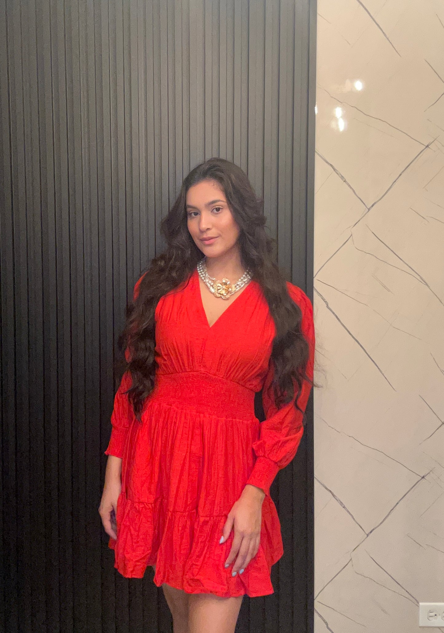 Woman in a red dress standing against a wall with a geometric pattern.
