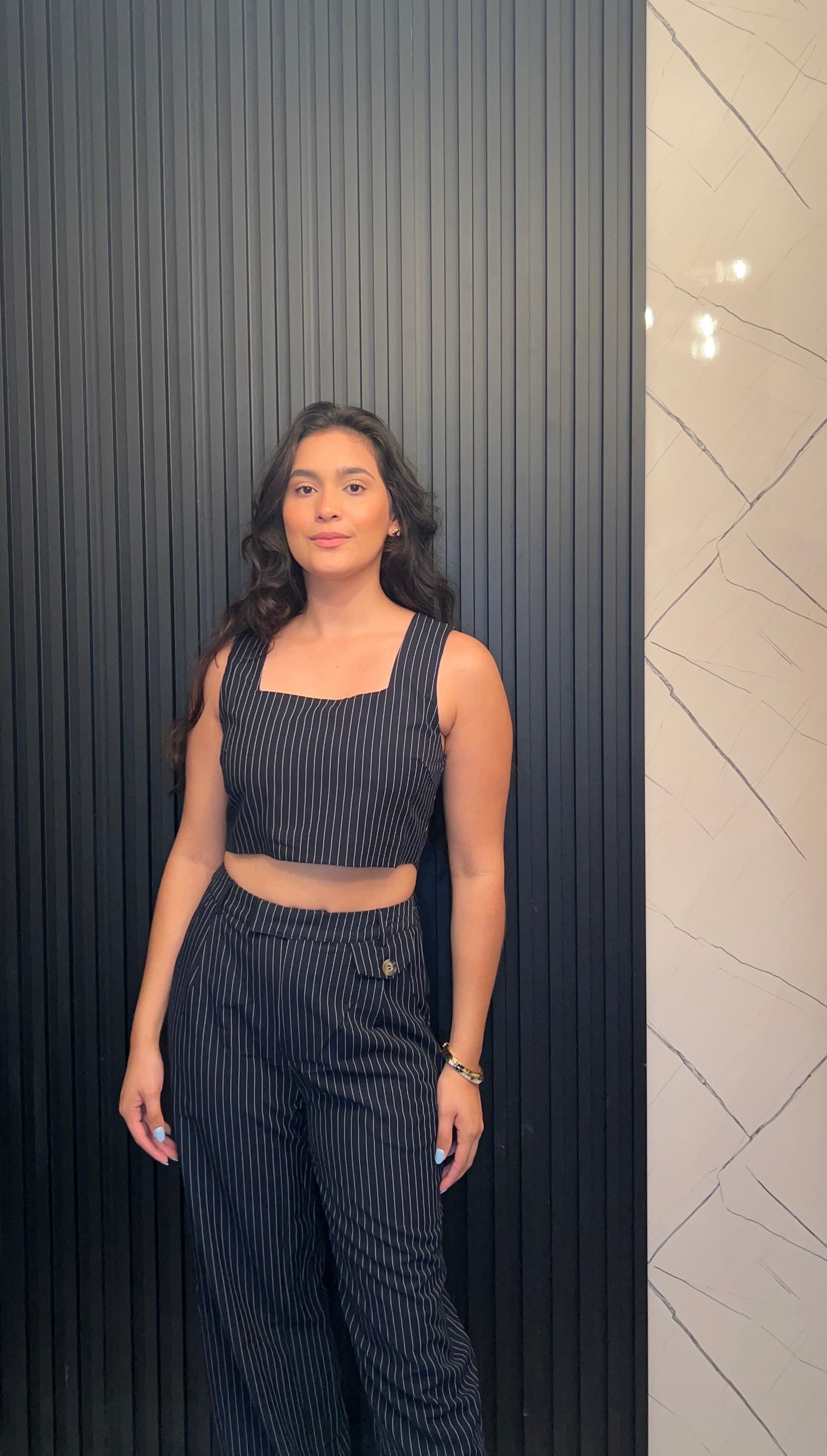 Woman in a black pinstripe outfit standing against a dark wall with a light patterned wall.