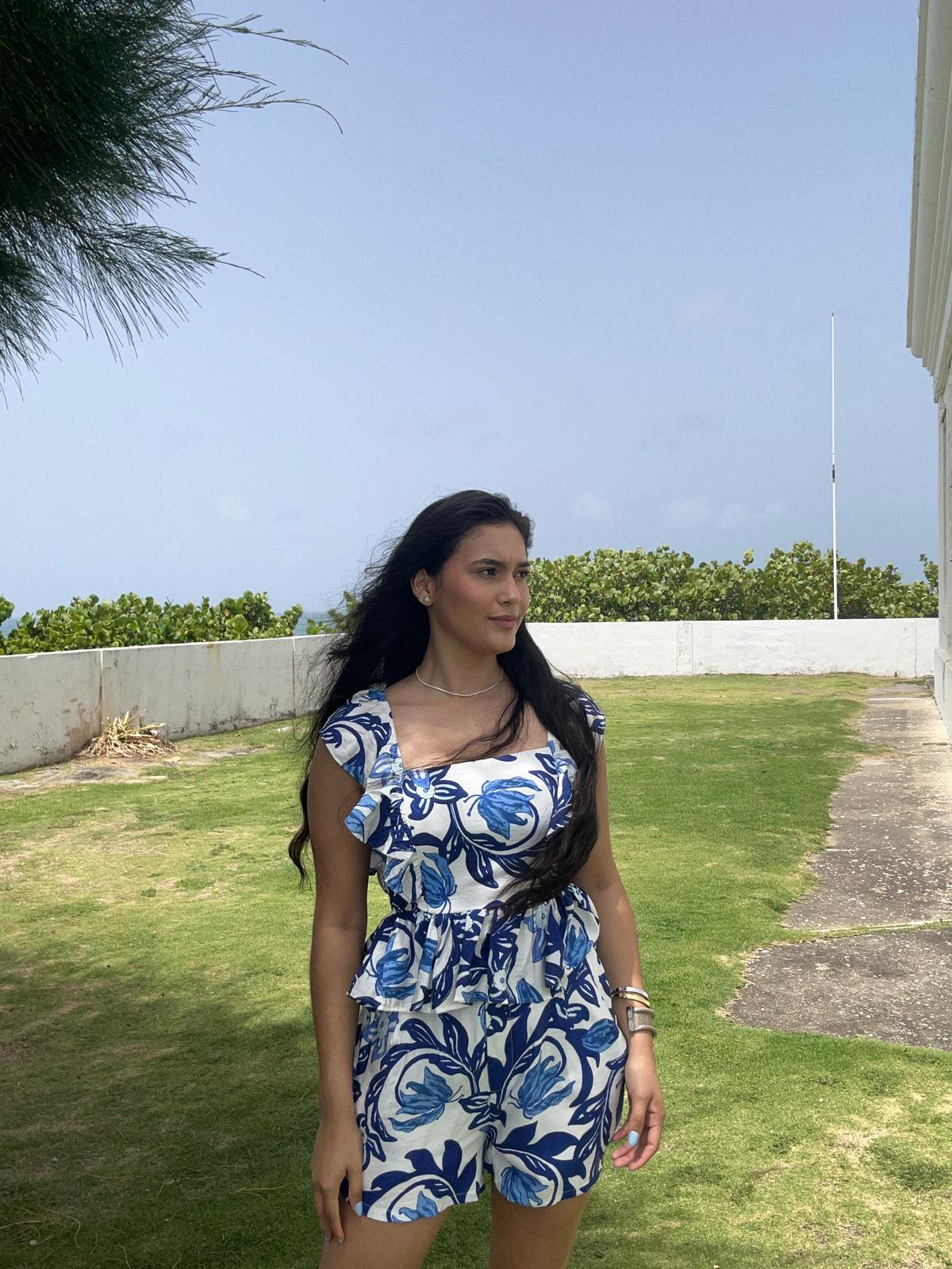 Woman wearing a blue and white floral dress standing on grass with a clear sky background