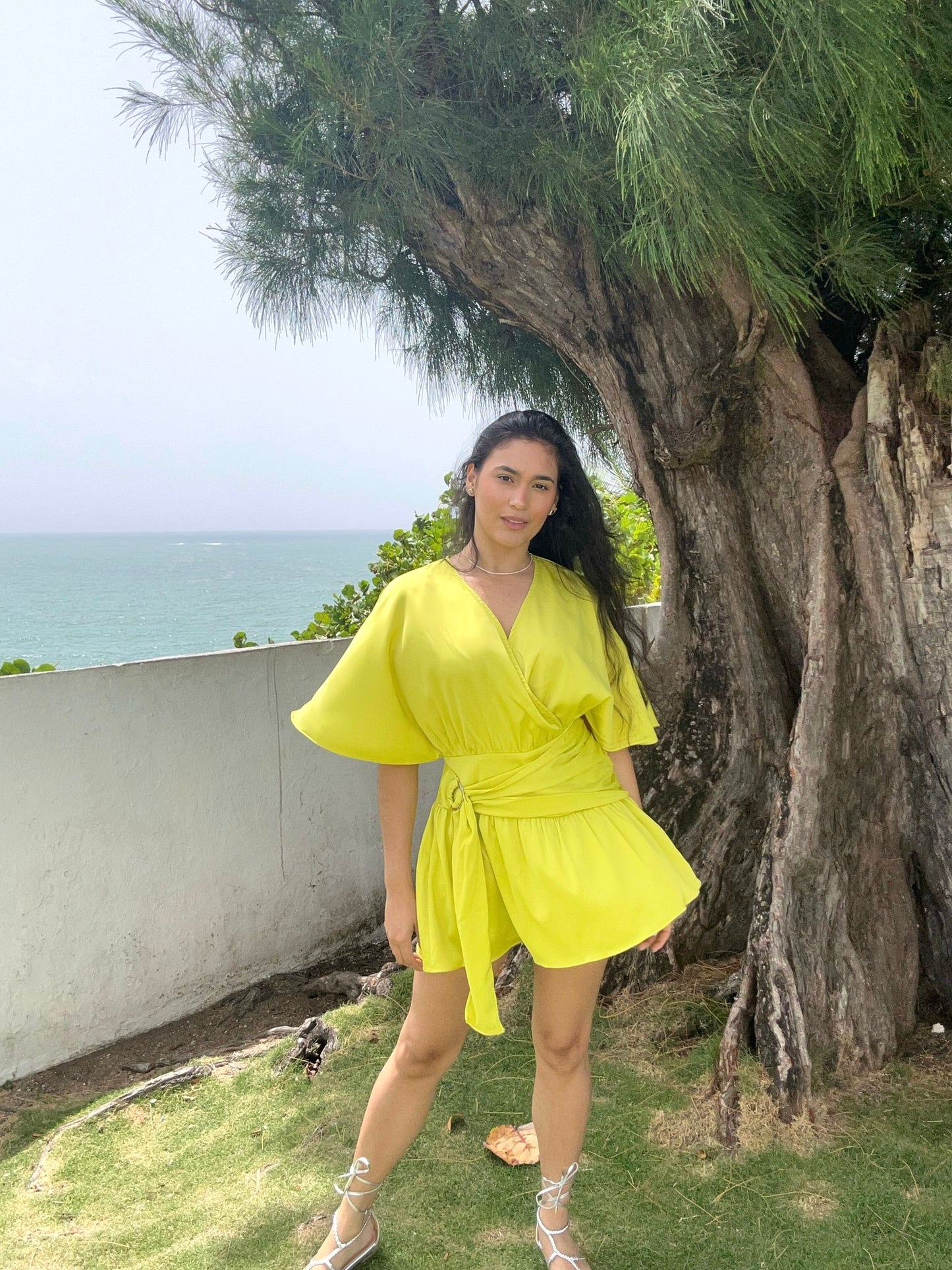 Woman in a yellow dress standing in front of a large tree with ocean view