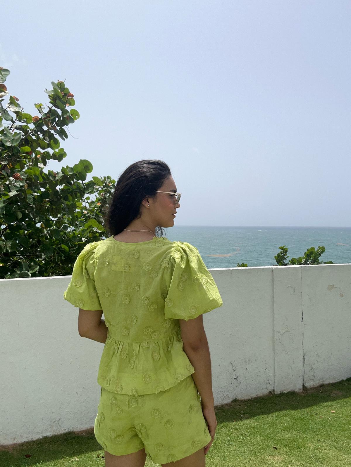Woman in a bright green outfit standing on a grassy area with a scenic ocean view.