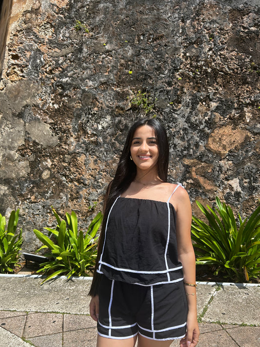 Woman in a black outfit standing in front of a stone wall with plants.