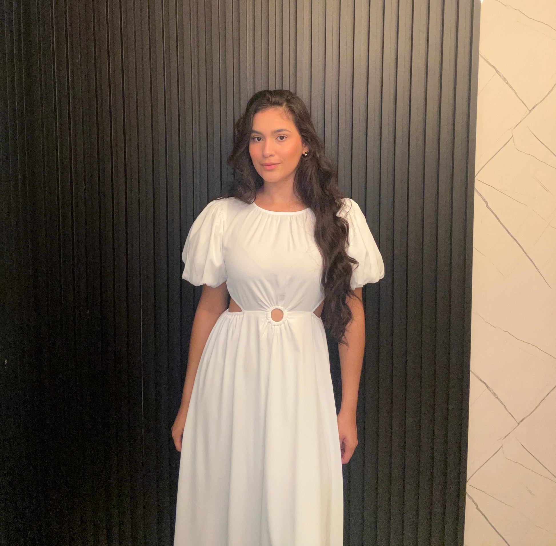 Woman in a white dress standing against a textured wall.