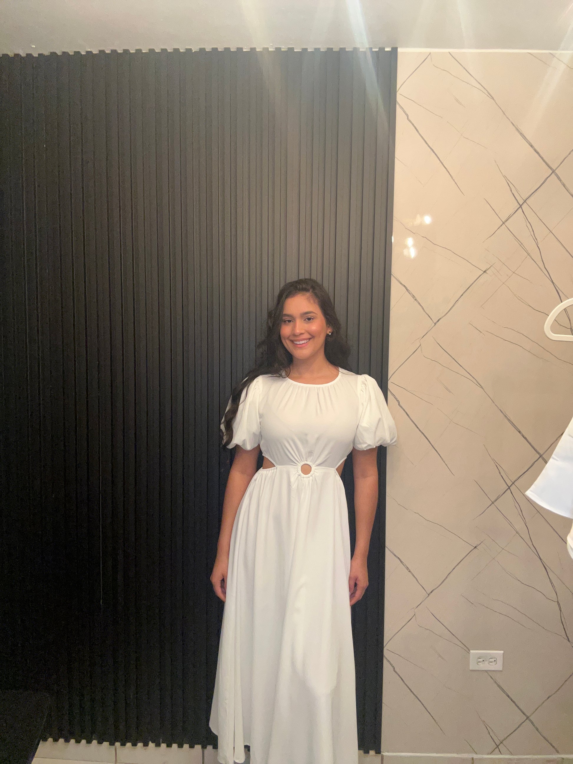 Woman in a white dress standing against a black and white striped wall.