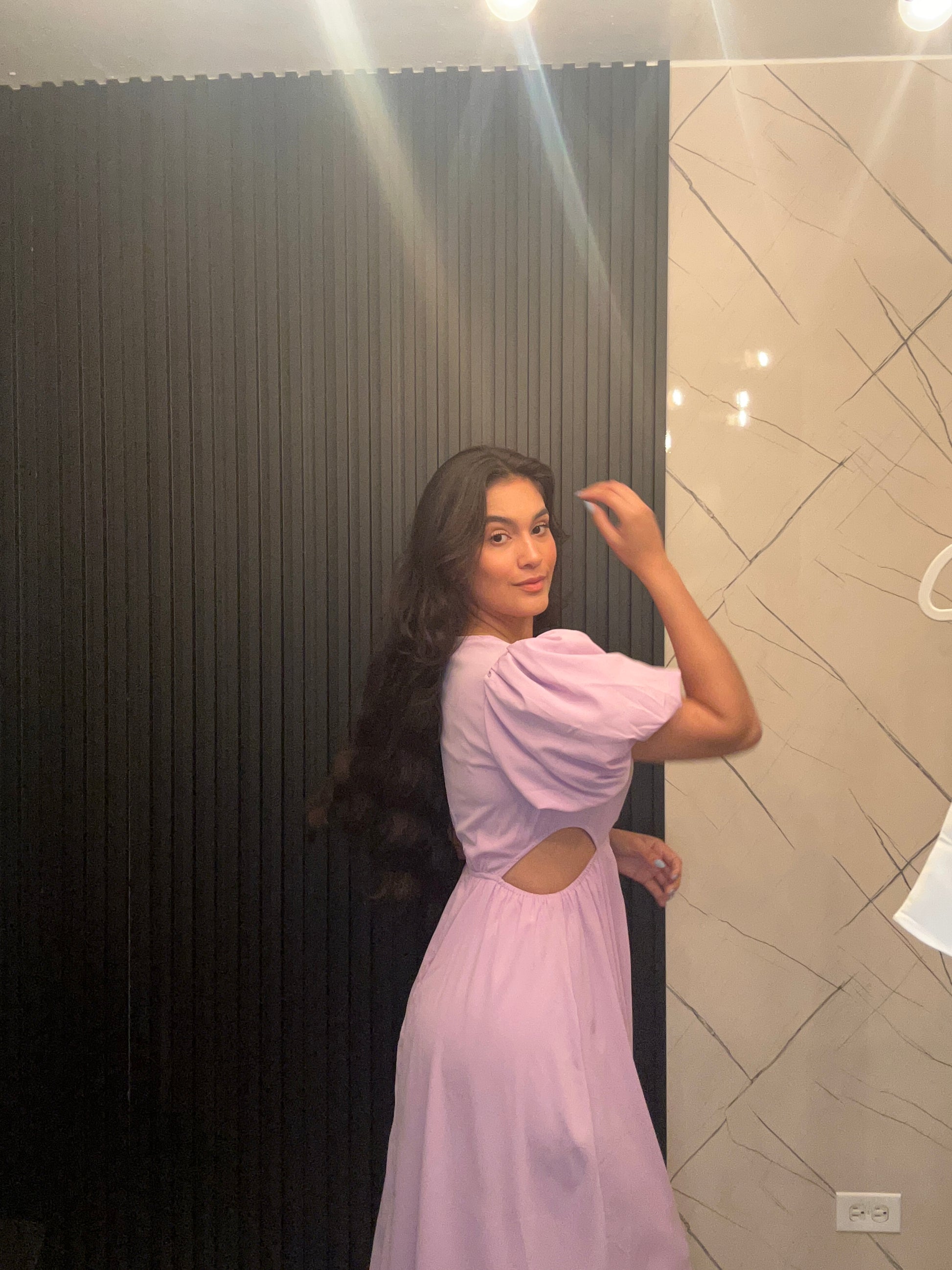 Person wearing a pink dress standing against a neutral wall.