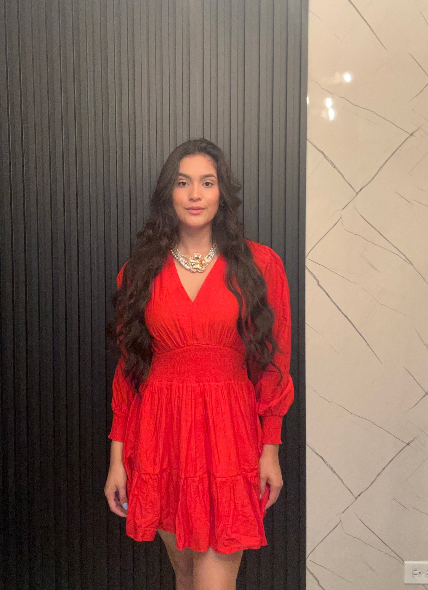 Woman wearing a red dress standing against a wall with a textured pattern.