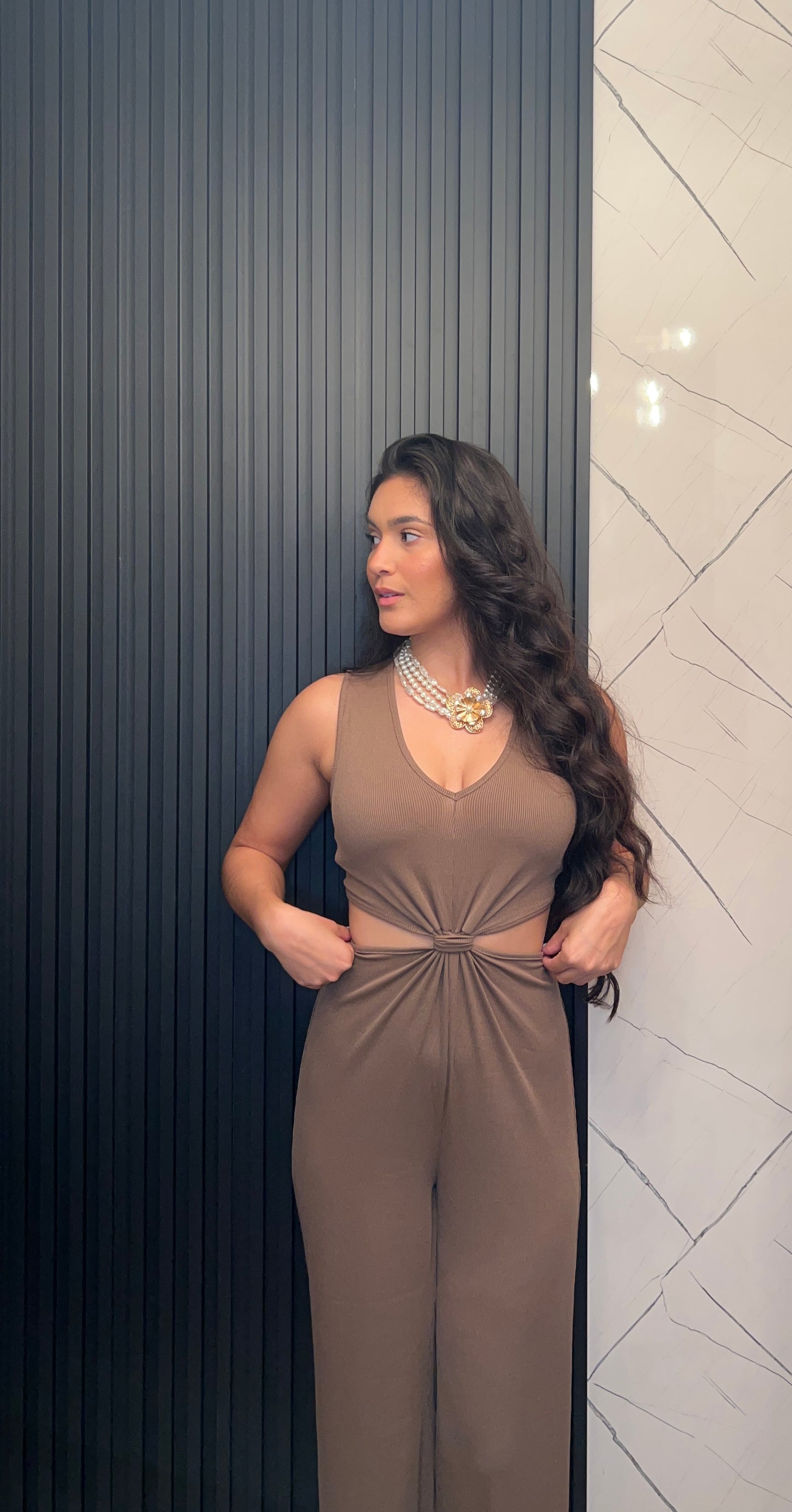 Woman wearing a brown jumpsuit standing against a textured wall.