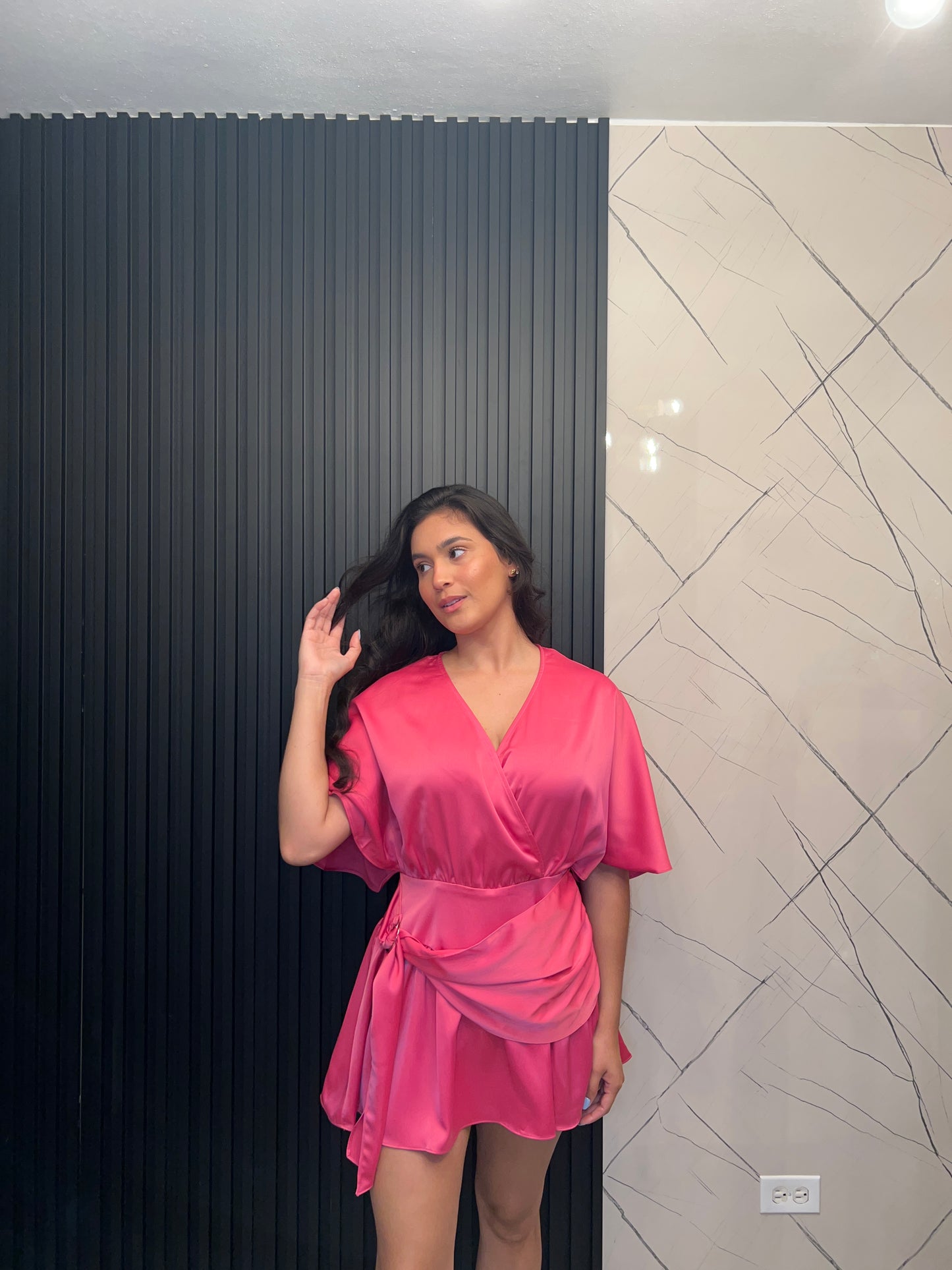 Woman in a pink dress lying on a black floor with a white wall and light fixture in the background