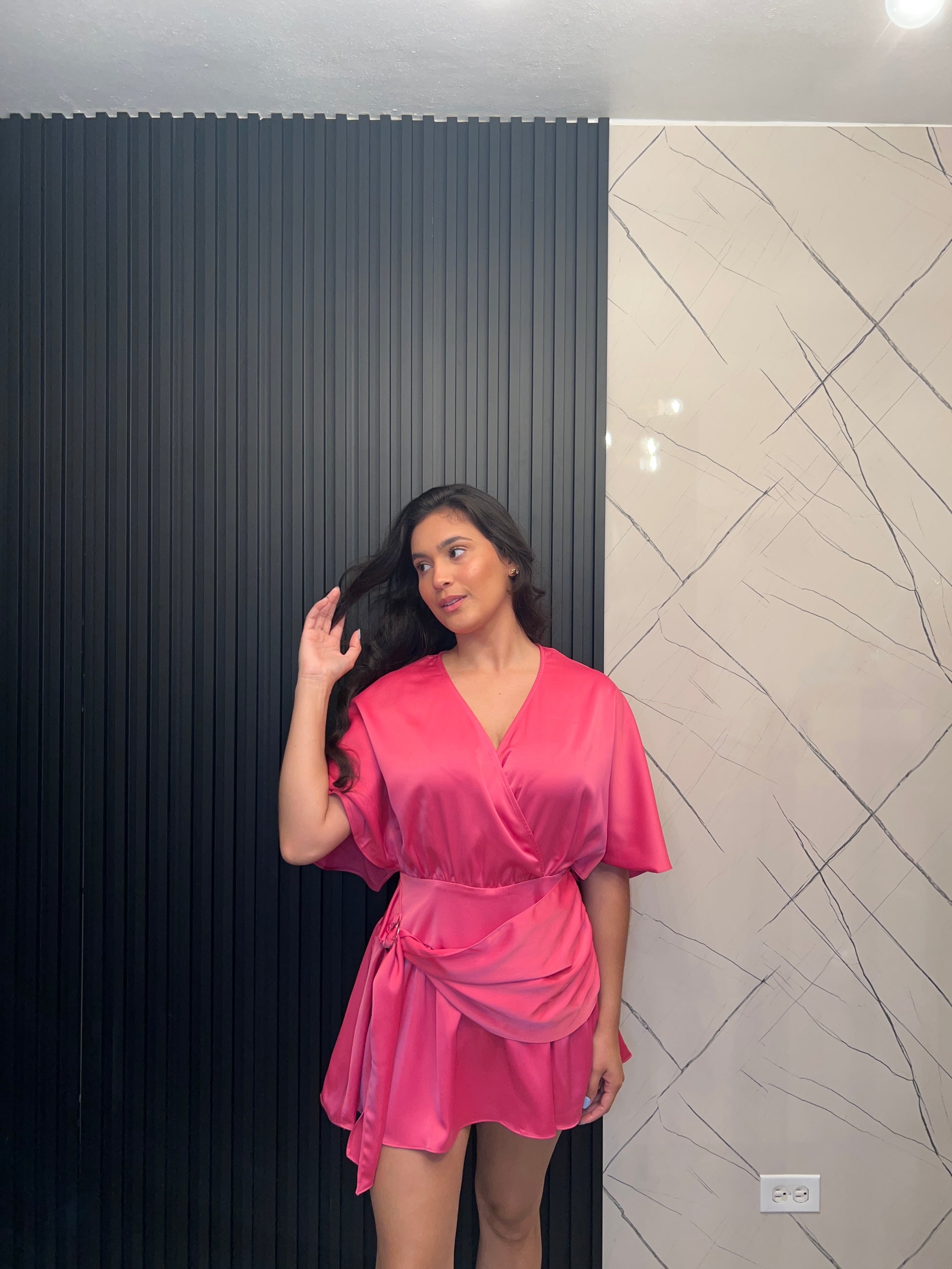 Woman in a pink dress lying on a black floor with a white wall and light fixture in the background