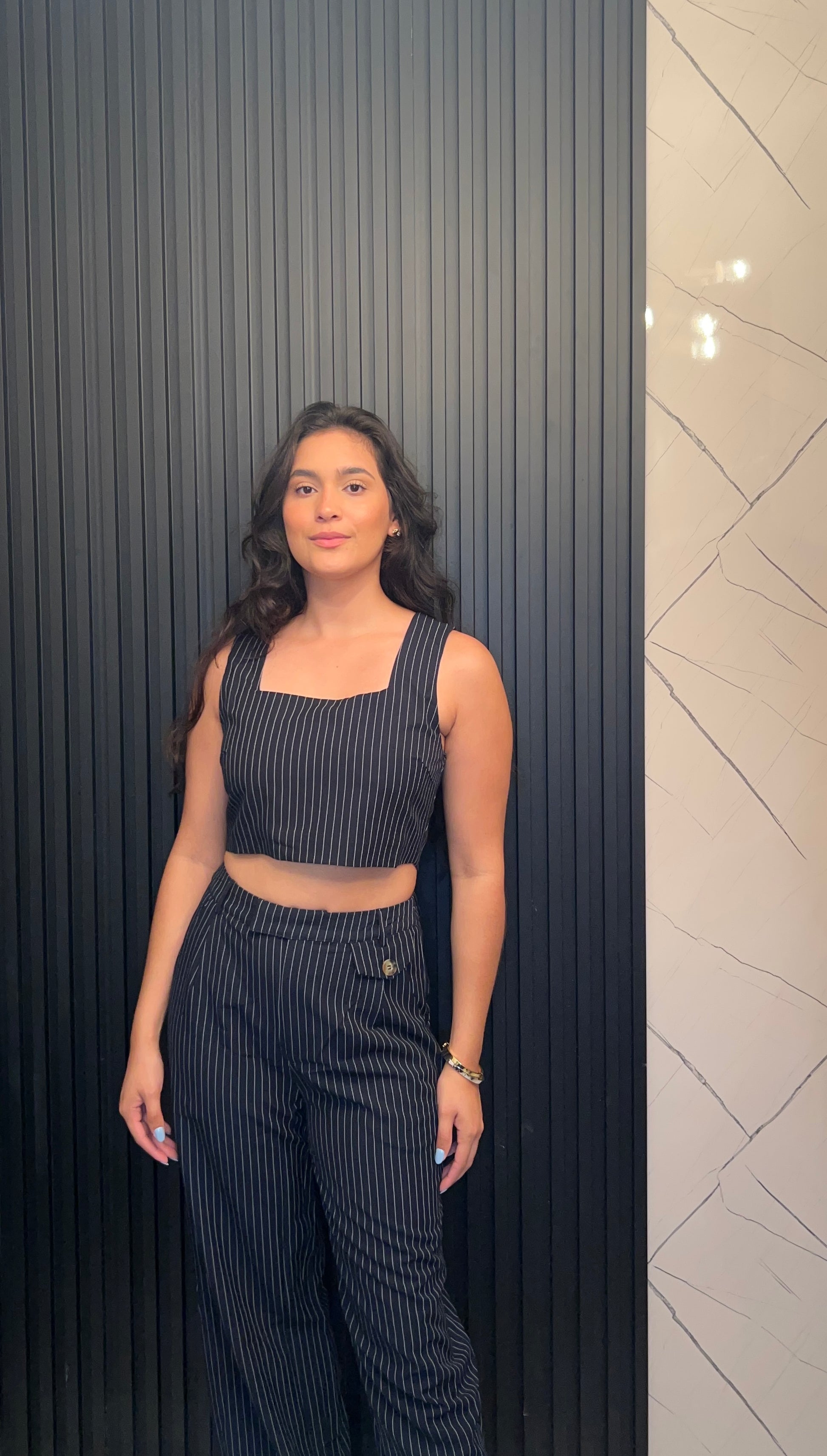 Woman in a black pinstripe outfit standing against a dark wall with a light patterned wall.
