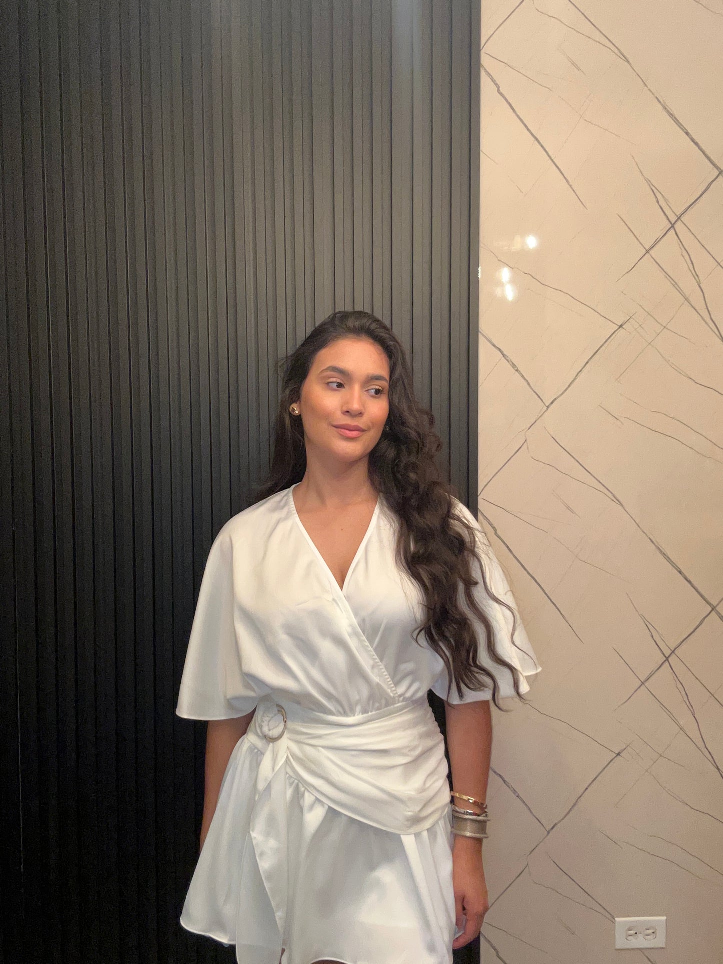 Person wearing a white outfit standing against a tiled wall.